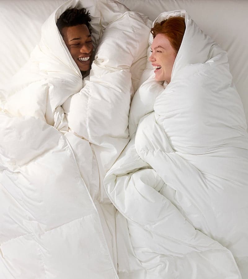 Two people laughing, wrapped in a white down comforter