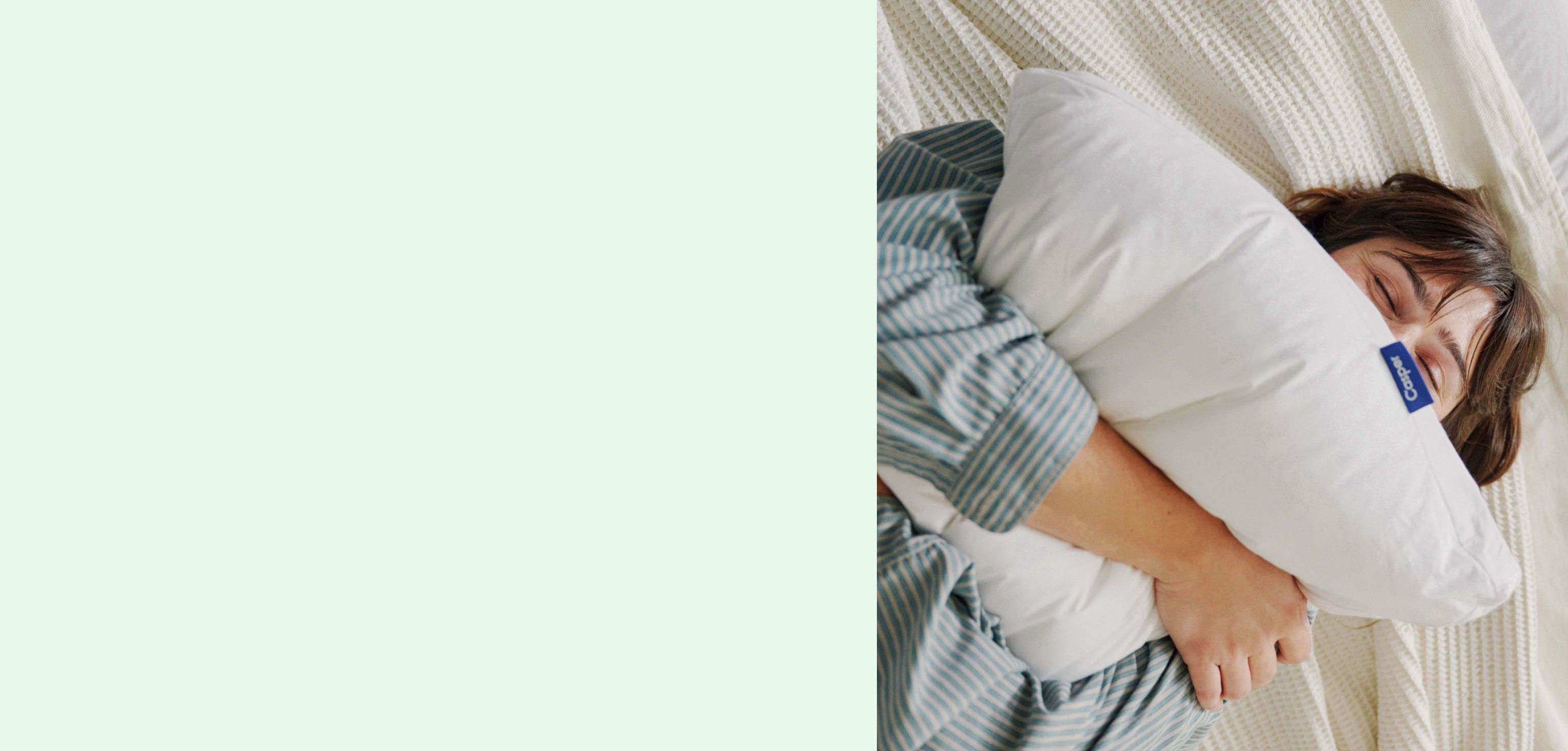 Light green background. Image of a woman squeezing a pillow in bed.