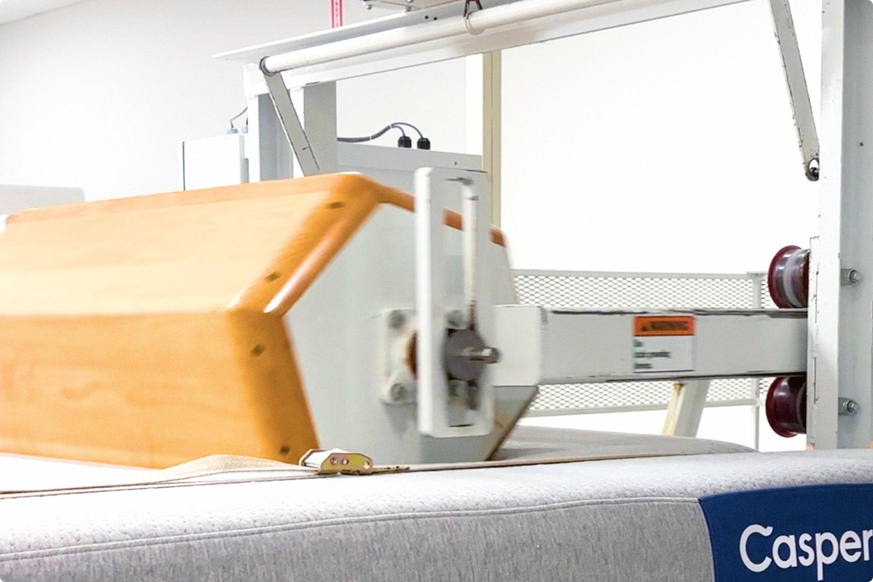 A Casper mattress in the manufacturing facility with a rolling machine on top to guarantee support