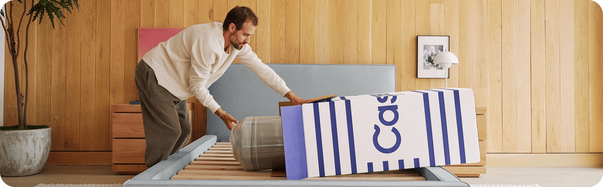A man unboxes his Casper mattress on his bed frame.