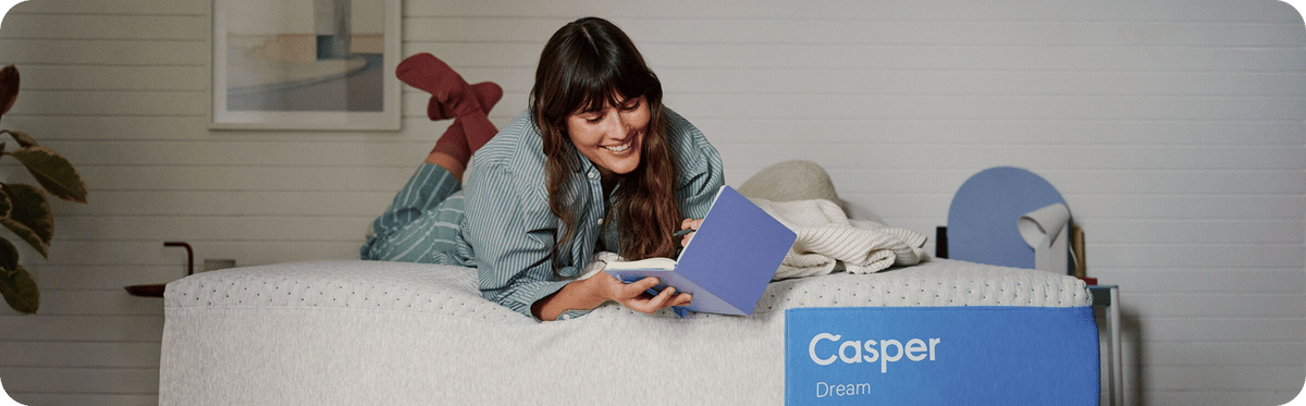 A woman writing in a book on her Casper Dream mattress.