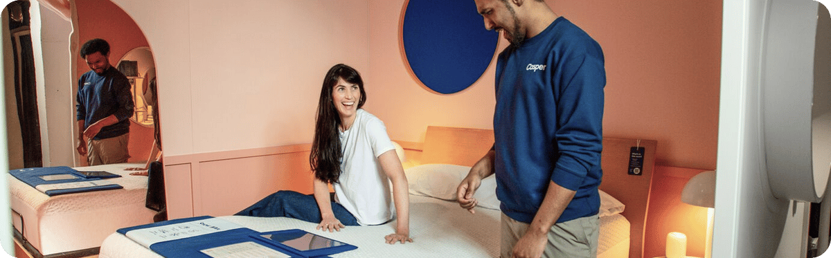A Casper store associate interacts with a person by a mattress.