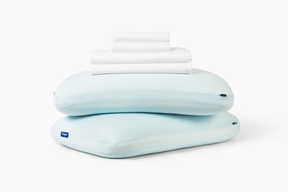 White sheet set, folded, stacked on top of two Hybrid Snow Pillows against a white background