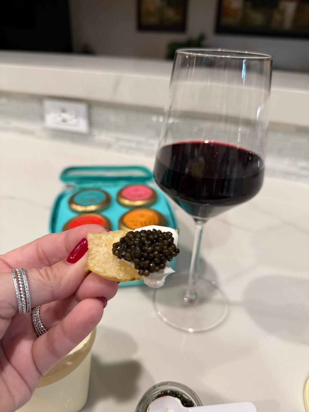 Customer's hand holding a cracker topped with Siberian Sturgeon Caviar next to a glass of red wine.