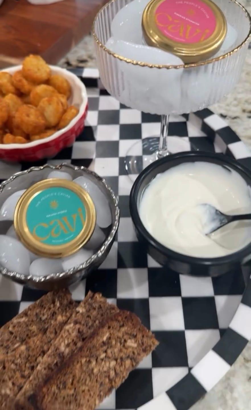Customer's Kaluga Hybrid Caviar tins in glass bowls, served with crème fraîche and crackers on a checkered tray.