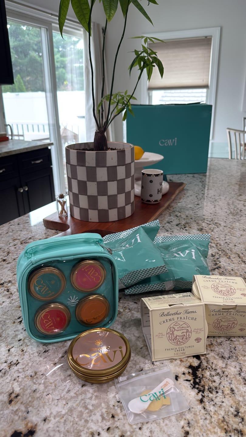 Customer's CAVI Tasting Kit Bag with caviar tins, crème fraîche, and accessories arranged on a granite countertop.