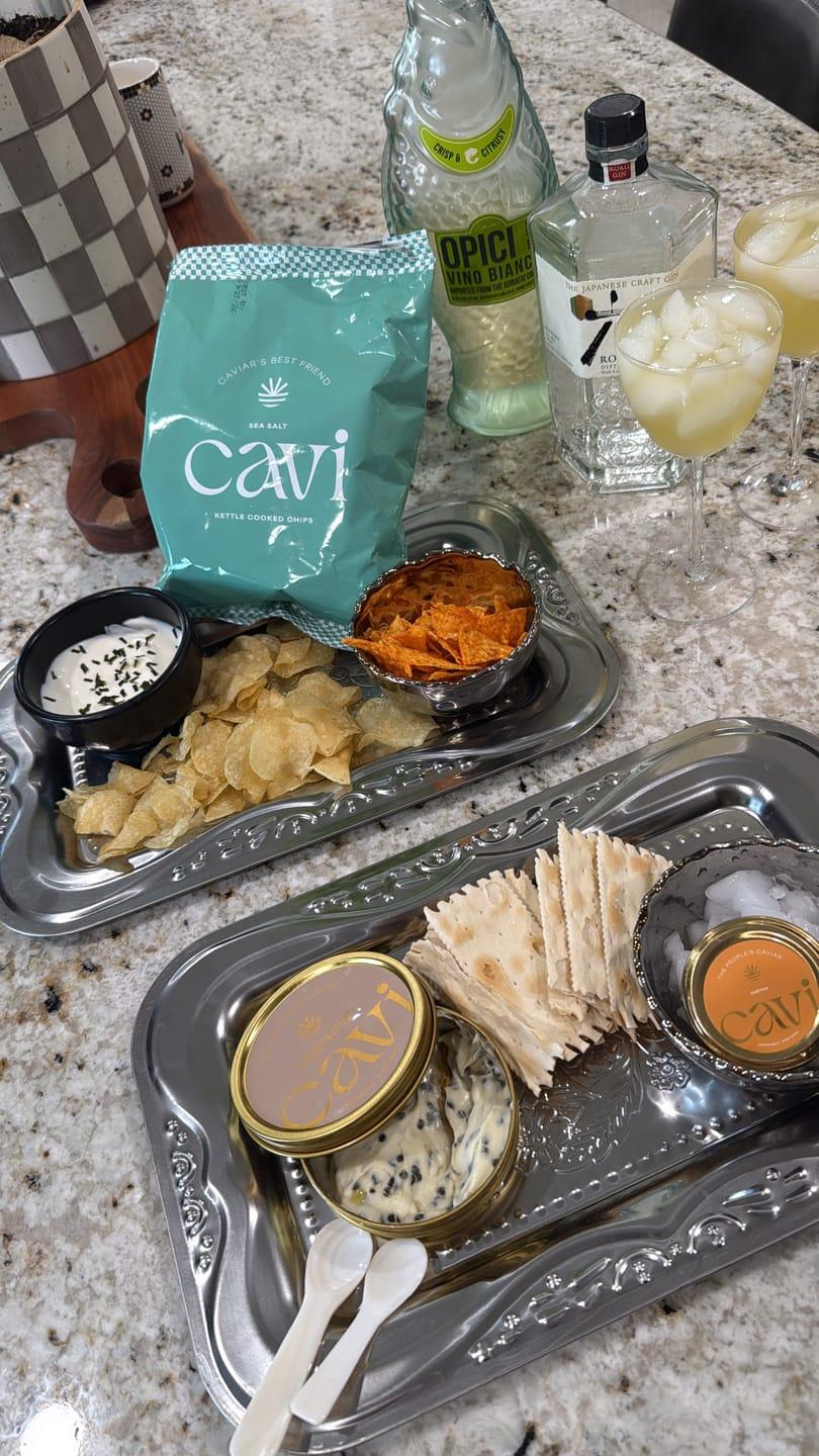 Customer's Osetra Caviar tasting kit featuring metal tins, crackers, and chips arranged on silver trays on a counter.