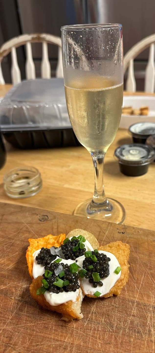 Customer's Kaluga Hybrid Caviar served on crispy appetizers with white cream and green garnish, next to a glass of wine.