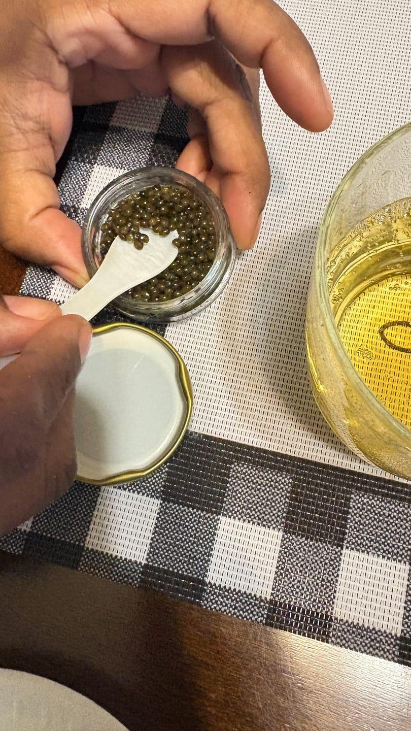 Close-up of a customer scooping caviar from a small glass jar with a spoon.