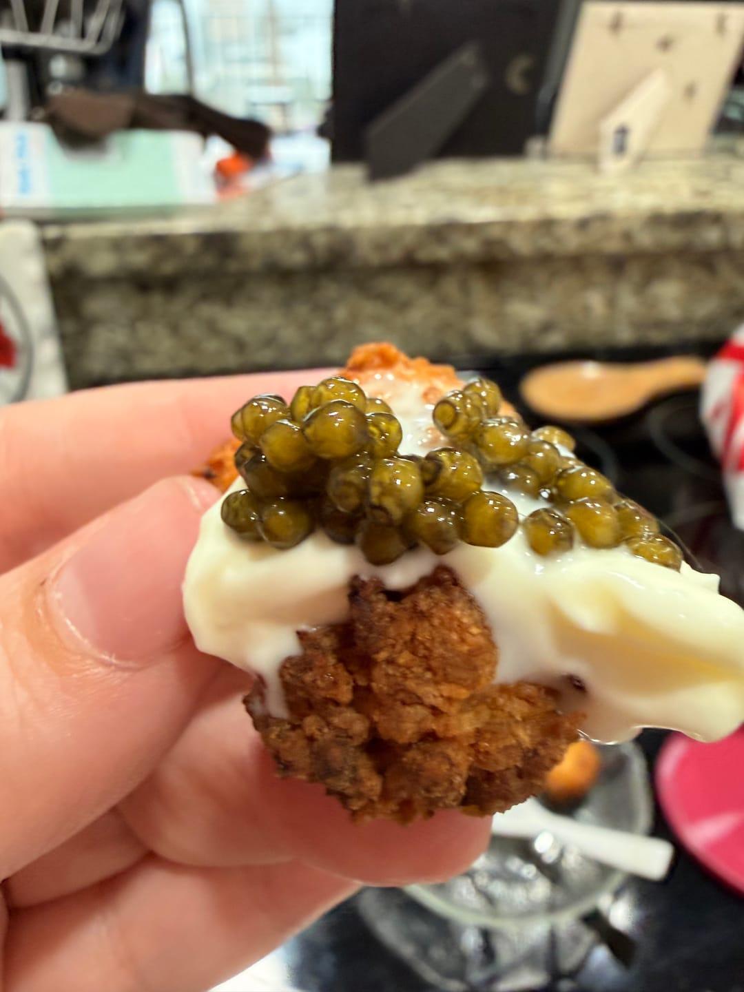 Close-up of a reviewer holding a fried bite topped with creamy Crème Fraîche and caviar.