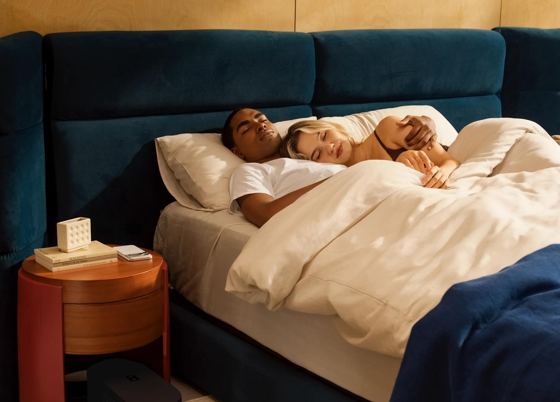 Two members asleep side by side, with the Pod Hub on the floor beside the bed