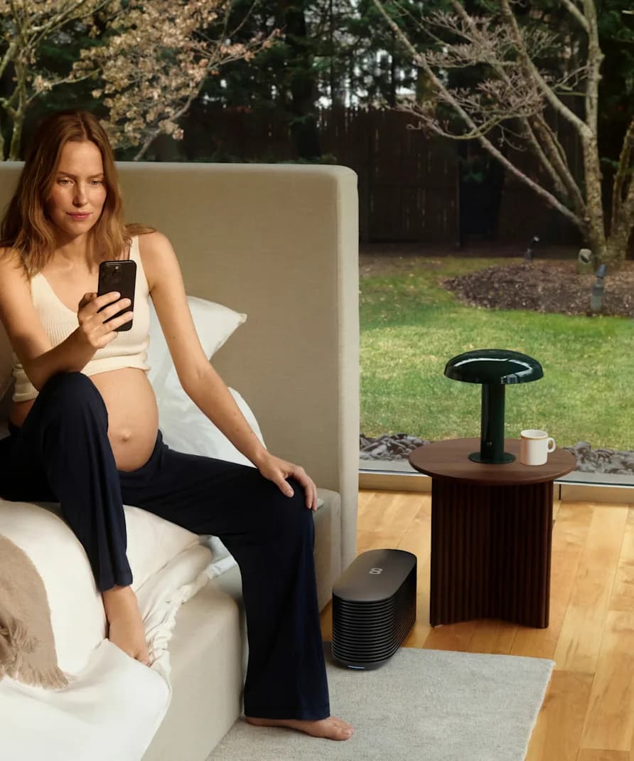 A pregnant woman sitting on the end of her bed