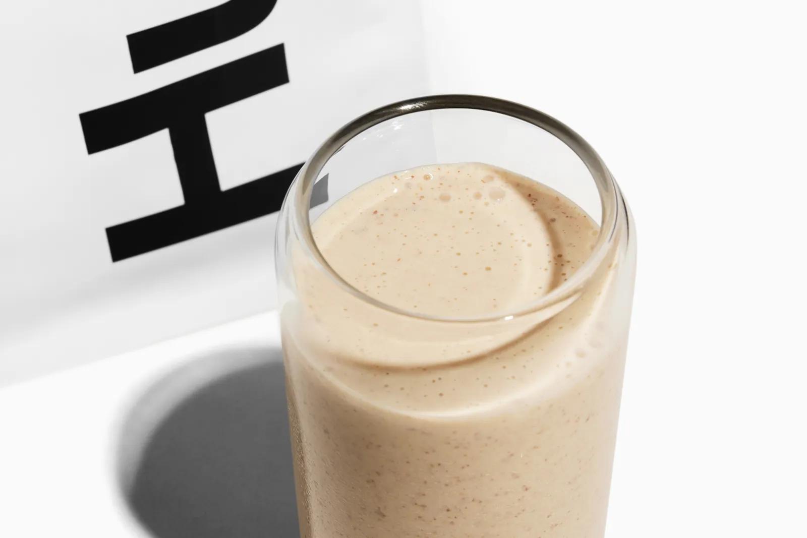 A glass of Huel shake next to a white bag of Huel Powder