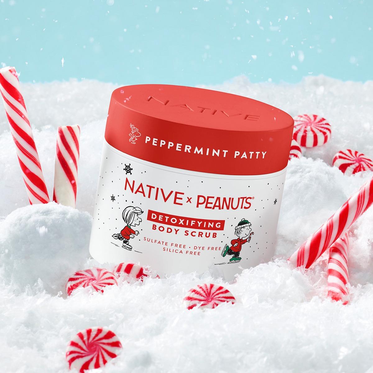 Native x Peanuts Detoxifying Body Scrub in a white jar with a red lid, styled in a snowy scene with candy canes against a light blue sky.