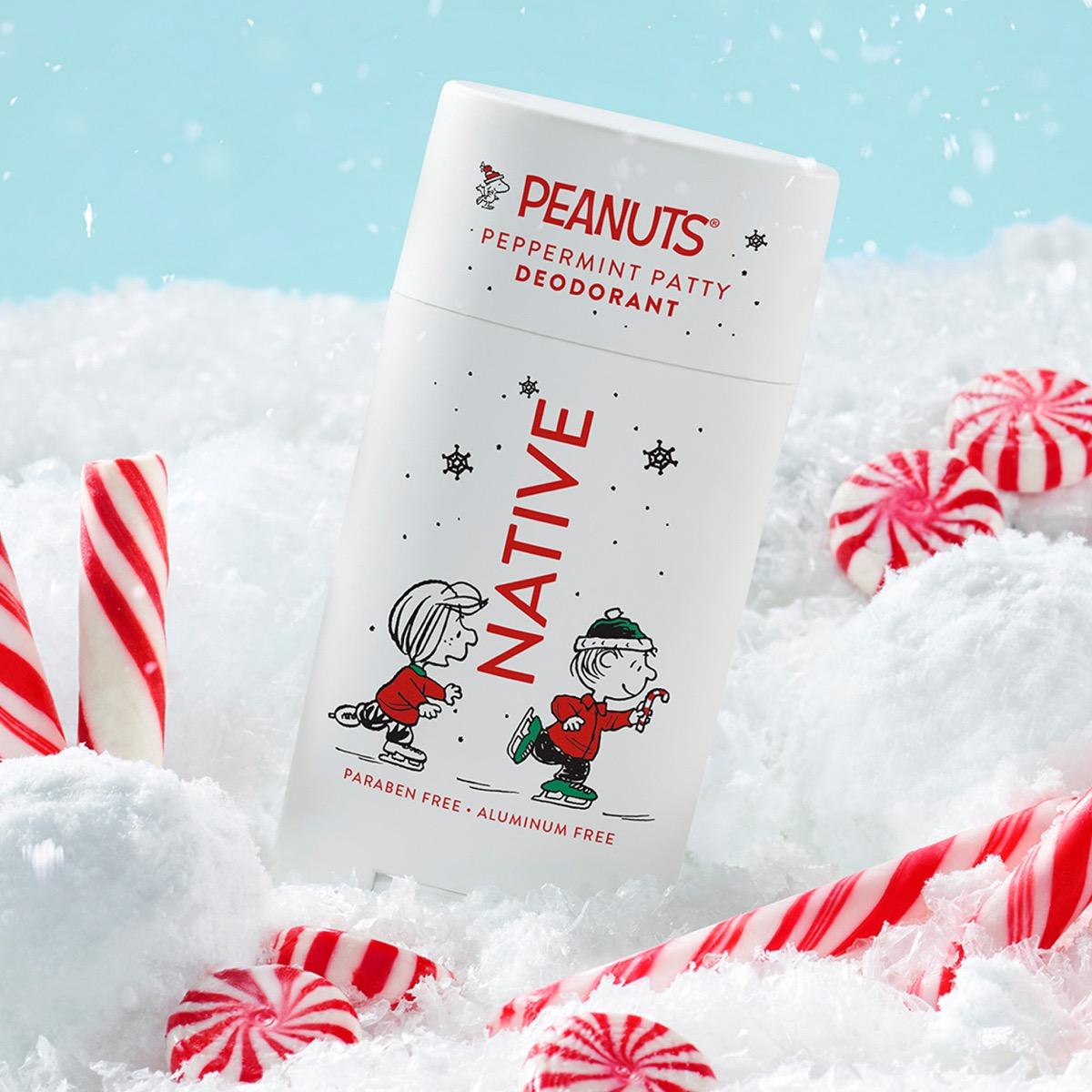 A can of Peanuts Peppermint Patty Deodorant standing in white snow with red-and-white candy canes around it. The can is white with red and black text and cartoon characters, set against a light blue background with falling snow effects.