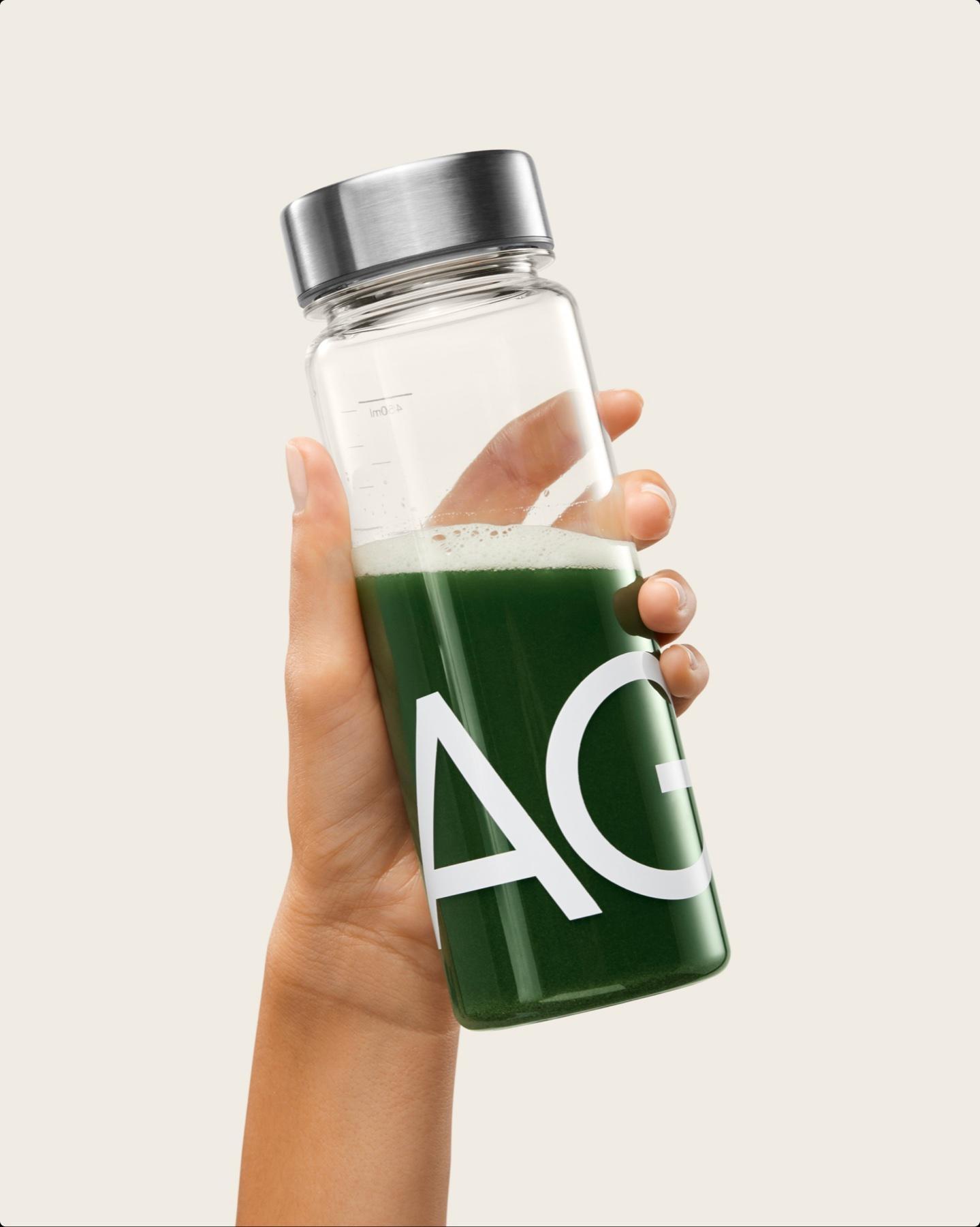 Hand holding a glass AG1 bottle filled with the green drink