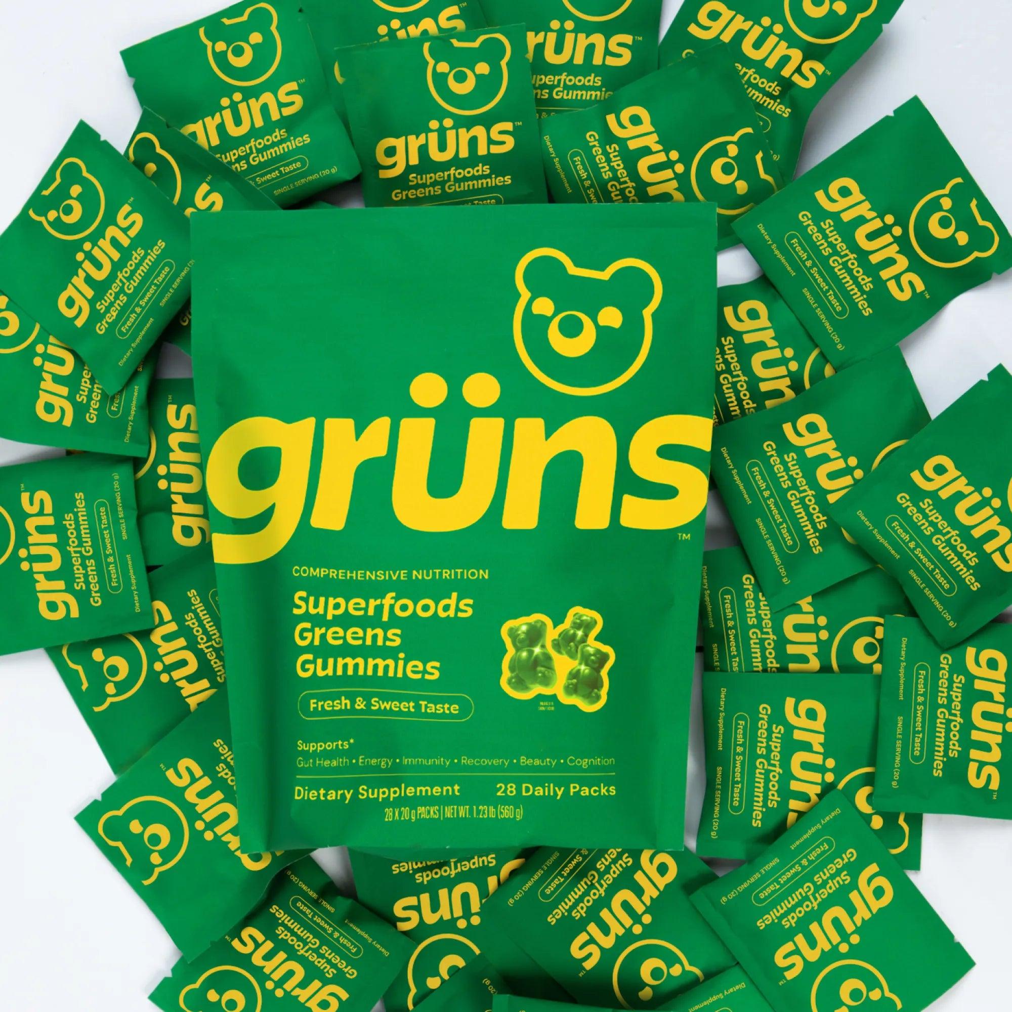 A Grüns Superfoods Greens Gummies pouch resting on a bed of green daily packets.