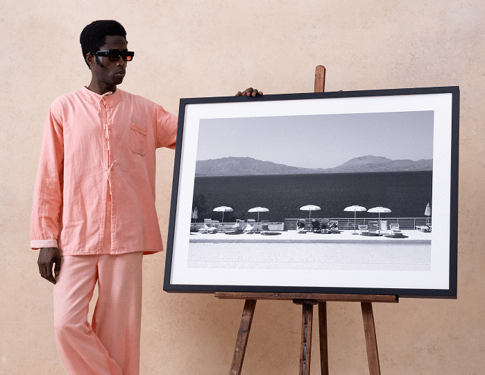 Model in pink beside a framed seascape print on a wooden easel