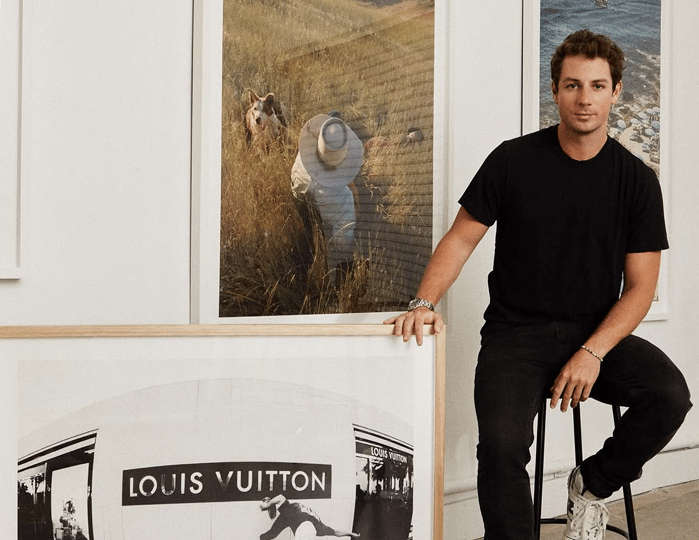 Max seated on a stool beside large framed prints