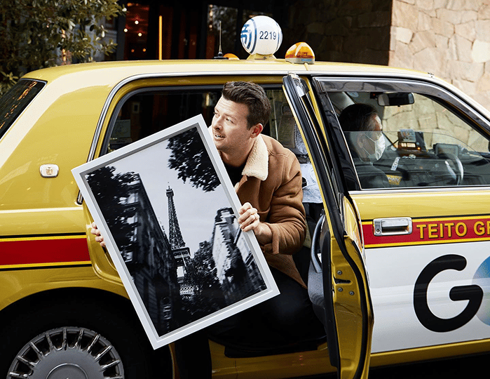 Man stepping out of a yellow taxi holding a framed black and white print