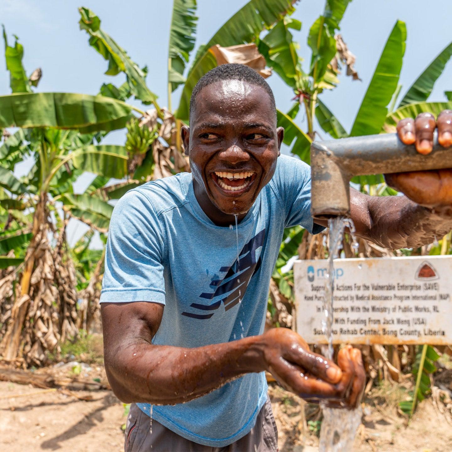 Smiling man rinsing his hands under a MAP International hand pump in Liberia