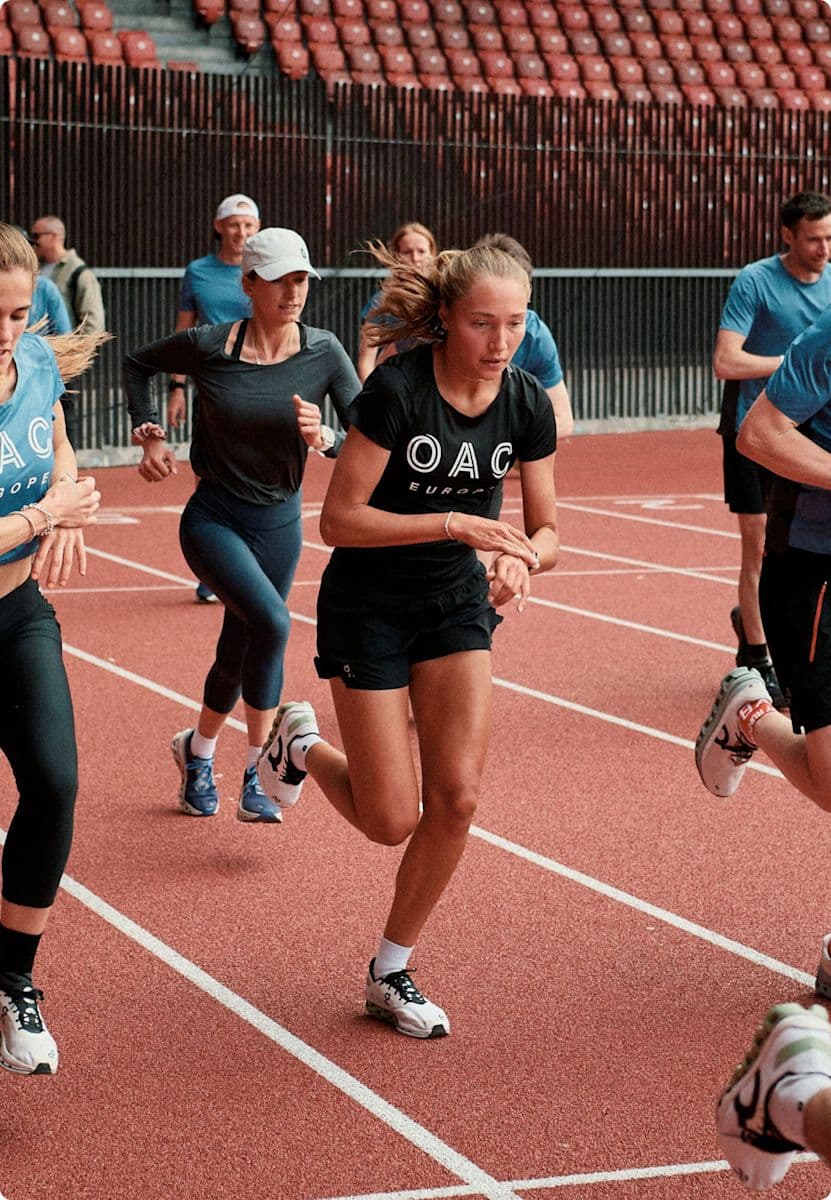 Woman in OAC shirt running among other athletes on an orange track.