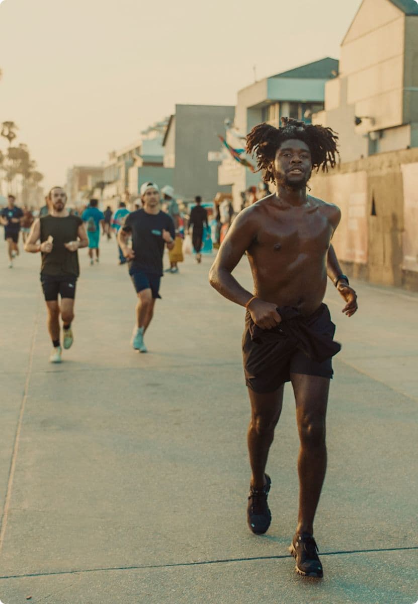 A shirtless man running on a boardwalk with other runners in the background.