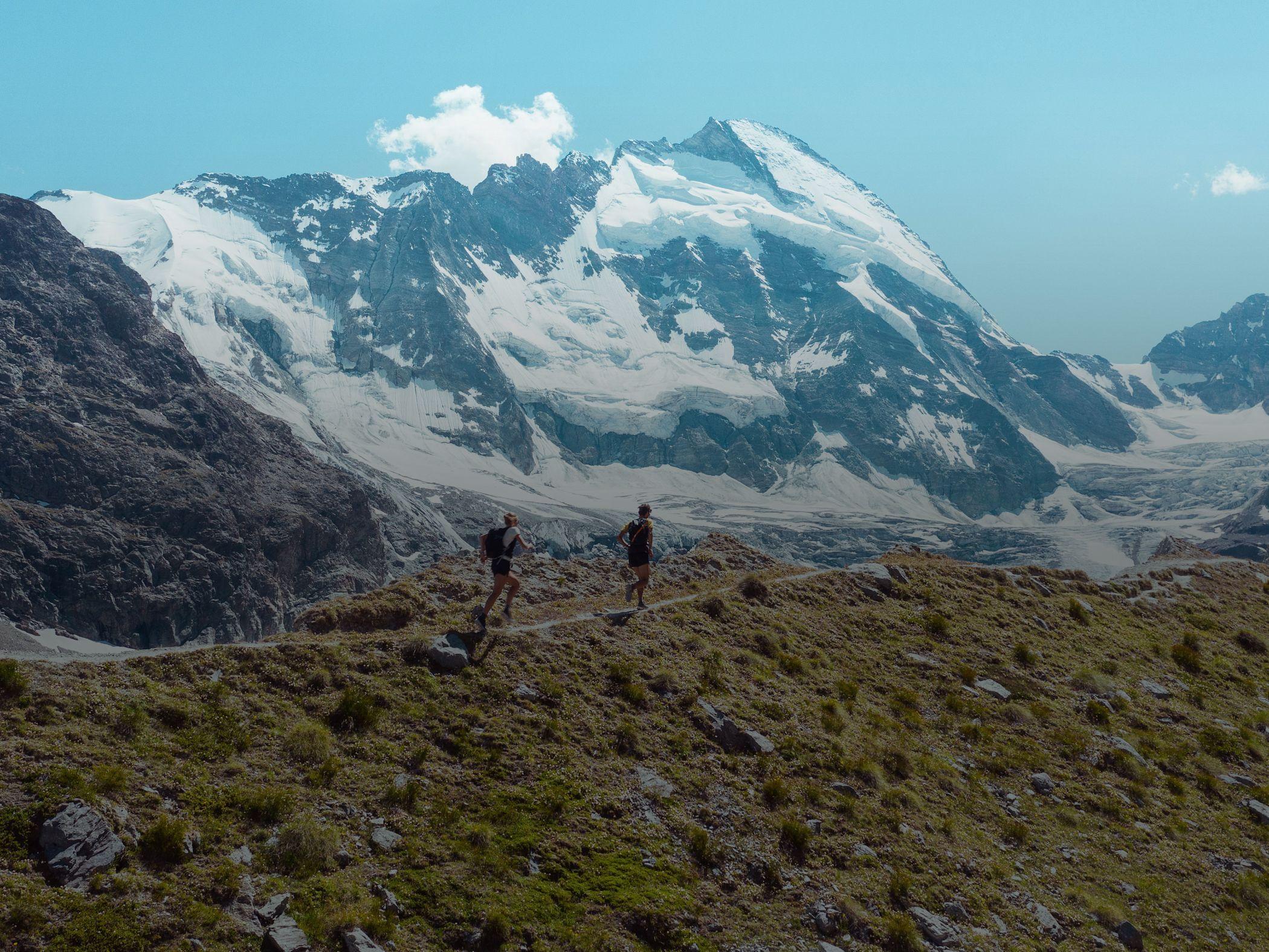 Two hikers walking through the Swiss Alps with snow-capped mountains in the background