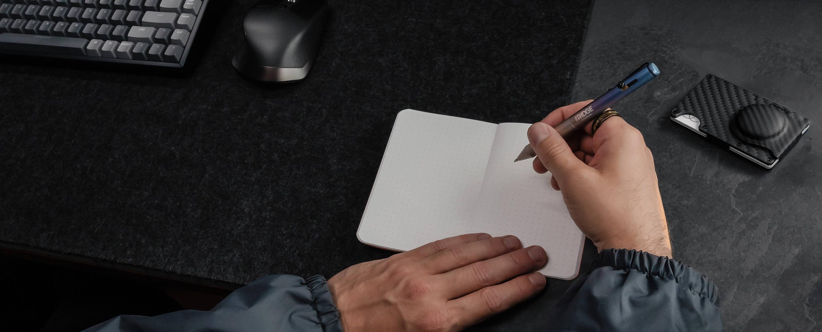 A hand writing in a notebook next to Ridge gear