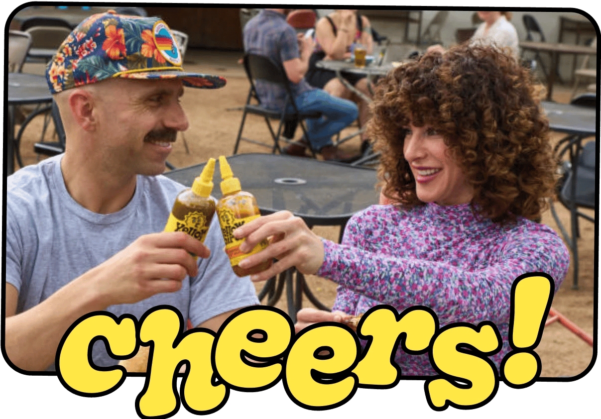 Erin and George, the Yellowbird co-founders, toasting with two bottles of hot sauce